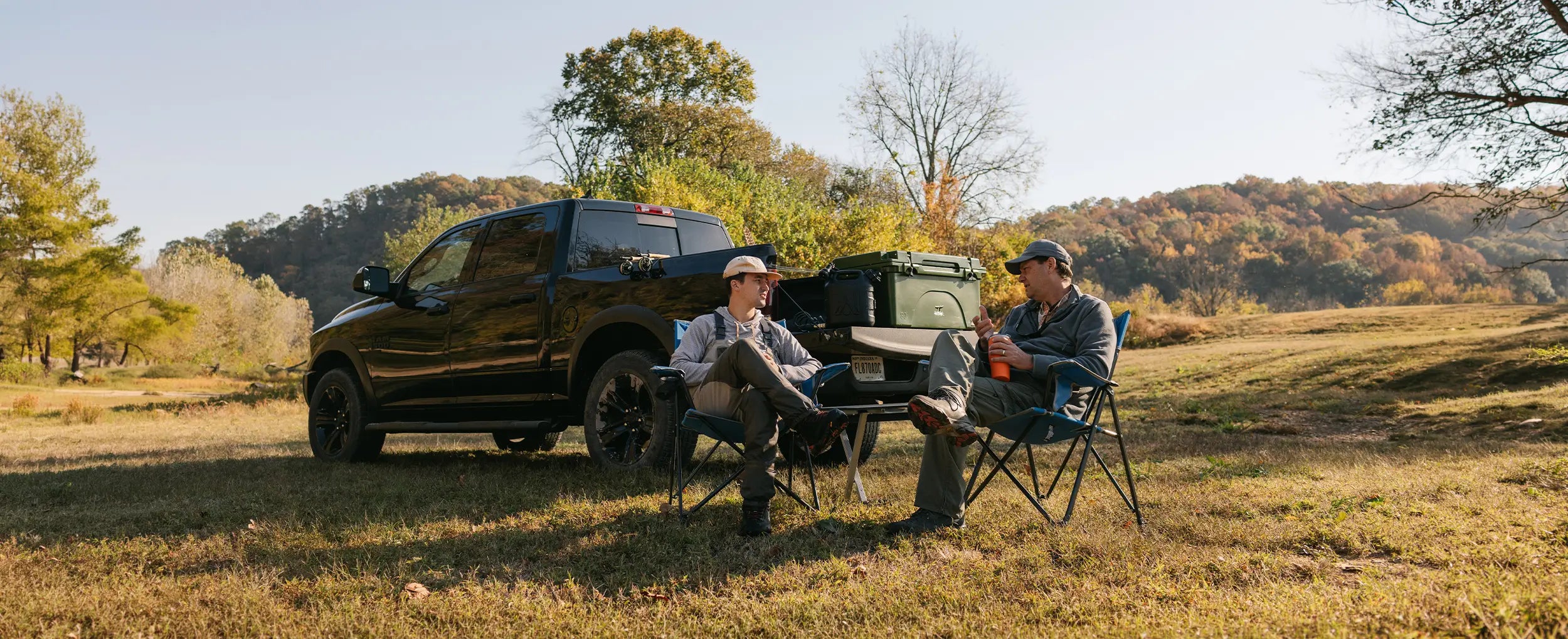 Two men sitting in stationary outdoor chairs beside a pickup truck.